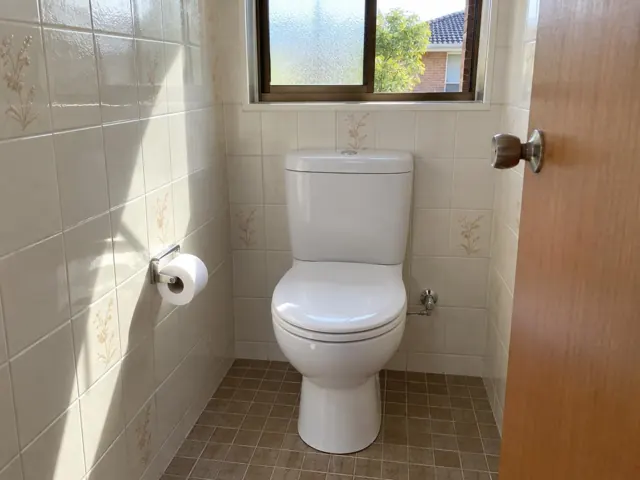 Clean white toilet in a tiled bathroom with a window and tiled floor in Melrose Park