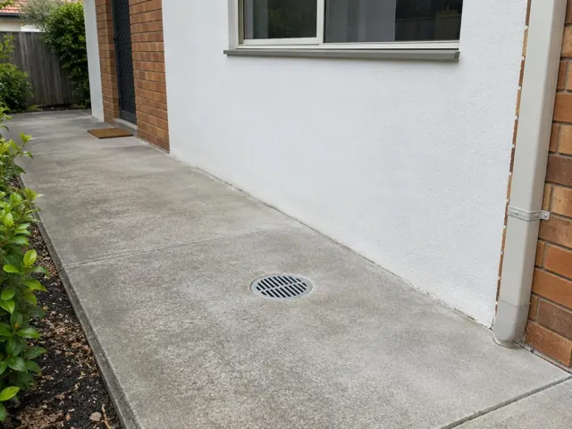 Concrete side path beside a brick and rendered house with a round drain grate in the paving in Ermington
